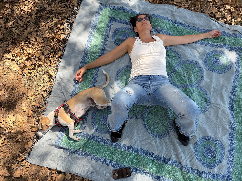 Marlene lying on a picnic blanket, eyes closed, arms outstretched and dog asleep at her side
