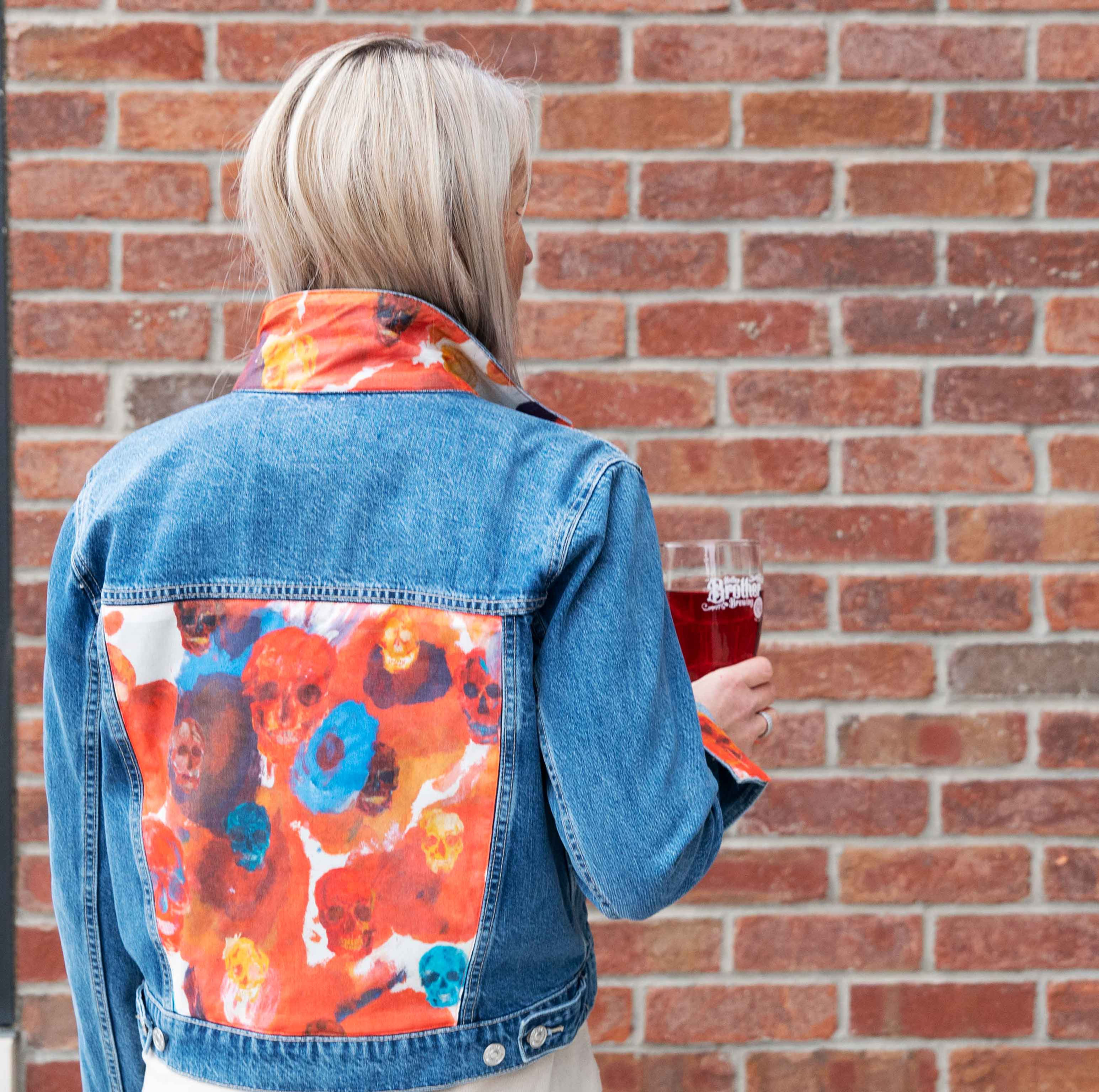 A woman stands at a brick wall wearing a jean jacket with an Alexander McQueen scarf sewn on it
