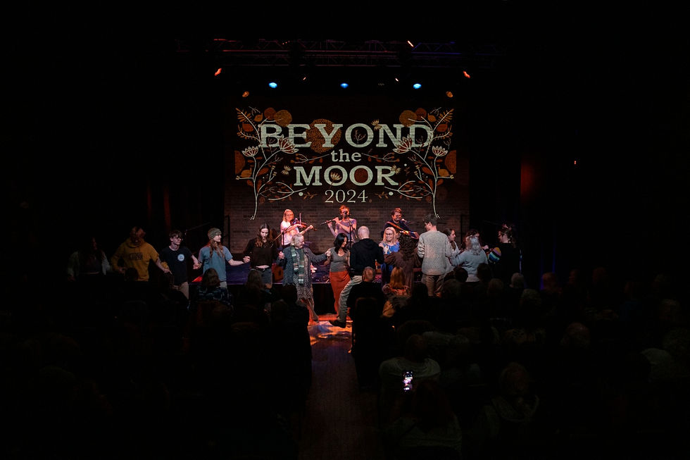 Audience dances in a dark theater before a stage with musicians and a backdrop reading BEYOND the MOOR 2024.
