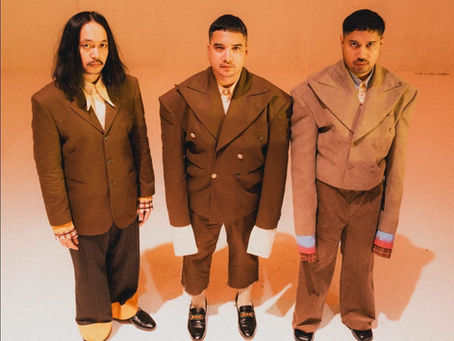Elephant Kind members in oversized brown suits stand against an orange wall, facing camera with serious expressions.