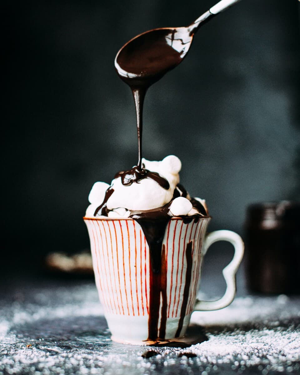 Chocolate sauce is drizzled onto a cup of hot cocoa