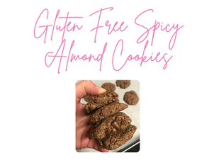 Hand holding gluten-free spicy almond cookies. Background shows more cookies. Pink script text above reads "Gluten Free Spicy Almond Cookies."