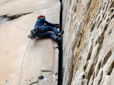 Grimpeur posant des coinceurs dans une fissure sur une grande voie de terrain d’aventure en montagne