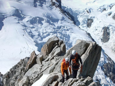 Un guide de haute montagne encorde une cordée sur une arête alpine enneigée, avec vue sur les sommets.