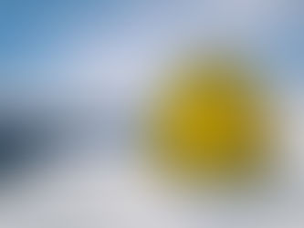Gelbe Sonnenfigur im Schnee vor Alpenpanorama mit klarem Himmel. Schneebedeckte Berge und Wälder im Hintergrund. Winterszenerie.
