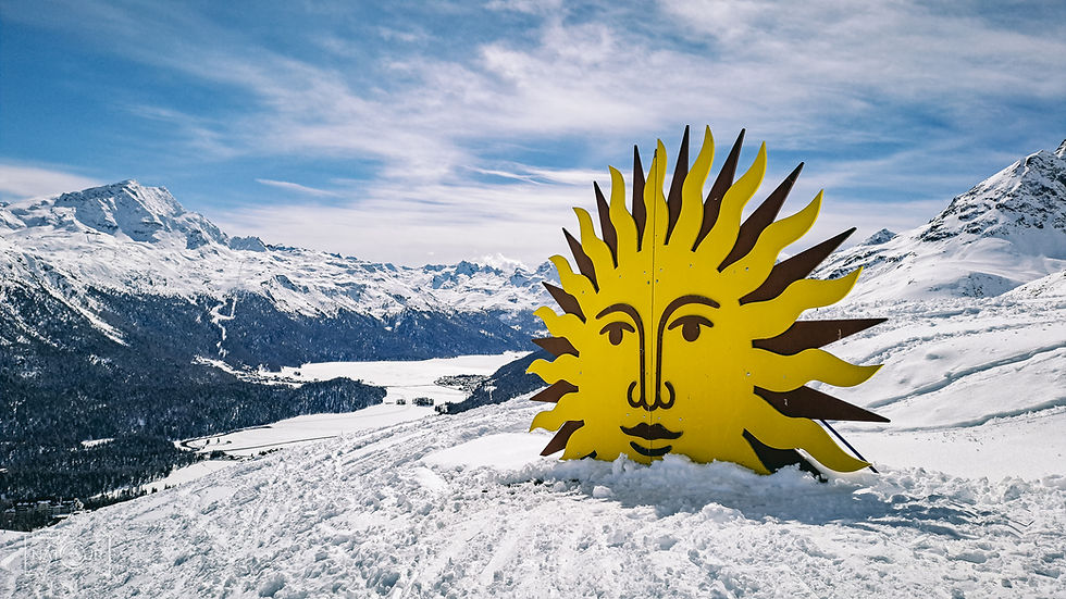Gelbe Sonnenfigur im Schnee vor Alpenpanorama mit klarem Himmel. Schneebedeckte Berge und Wälder im Hintergrund. Winterszenerie.