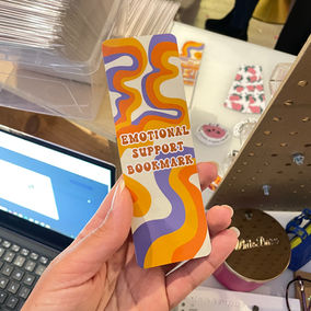 a funky orange and purple bookmark with "emotional support bookmark" written on it. 70s theme