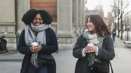 two women walking and smiling while drinking coffee