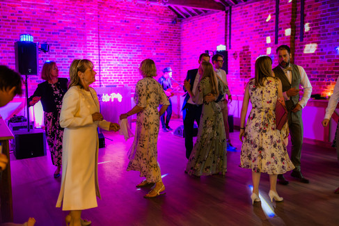 Guests dance at a wedding reception, in a room with pink lighting.