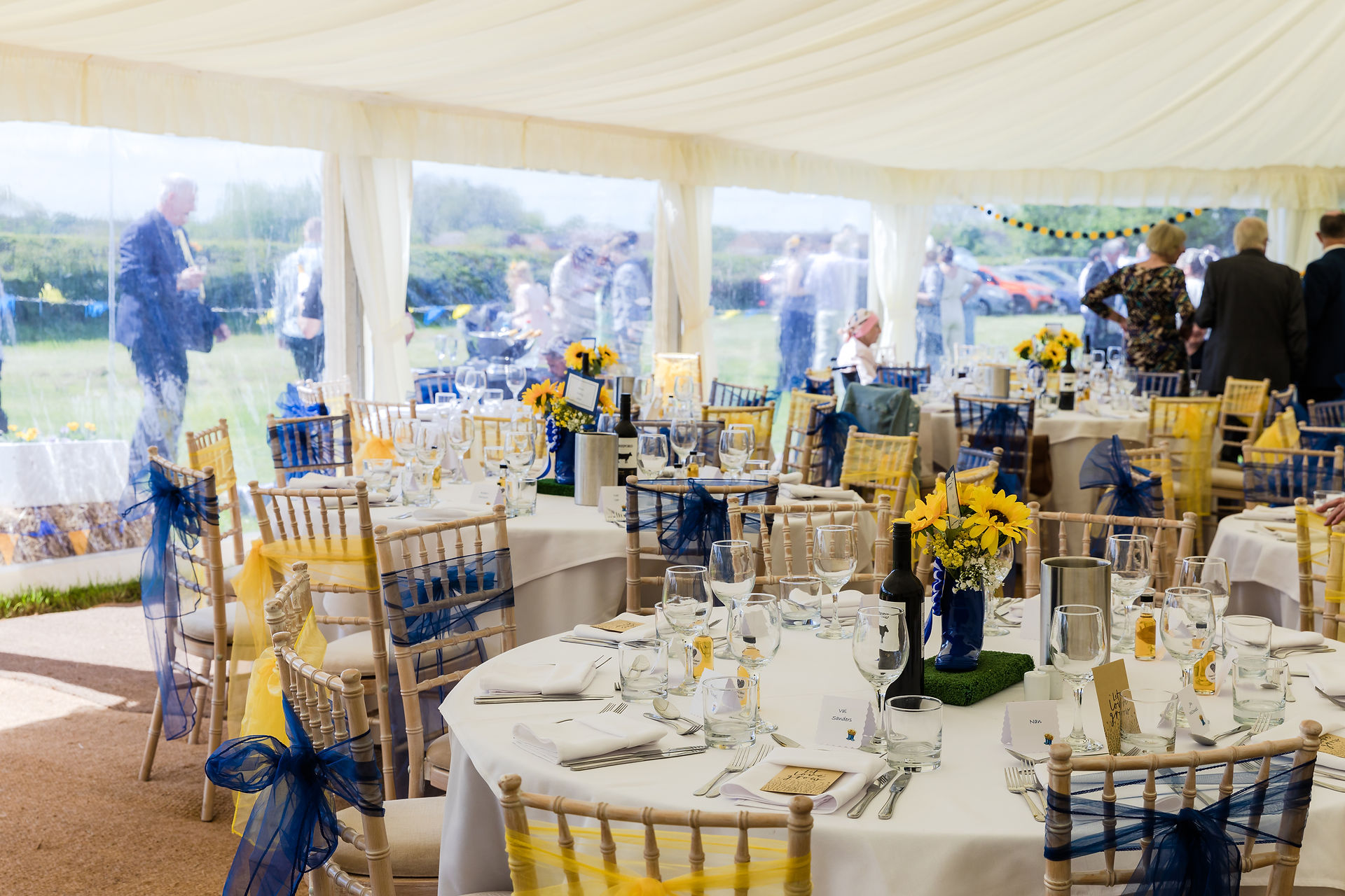 Elegant event tent with tables, chairs, sunflowers, and guests visible outside