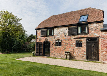 Rustic brick building with open doors and windows in a grassy setting.