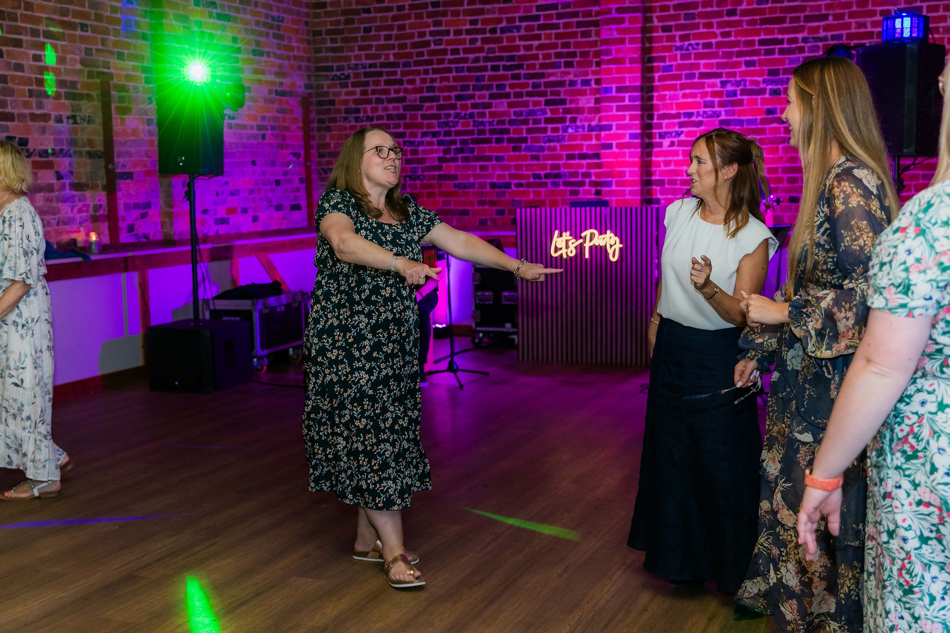 Dancing woman points to 'DJ Party' sign, enjoying the wedding reception with friends.