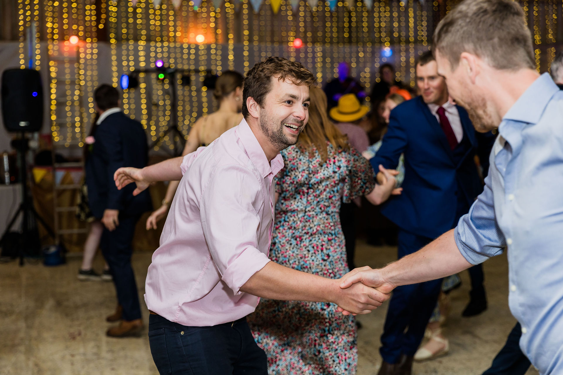 Man in pink shirt dancing with others, wedding reception celebration