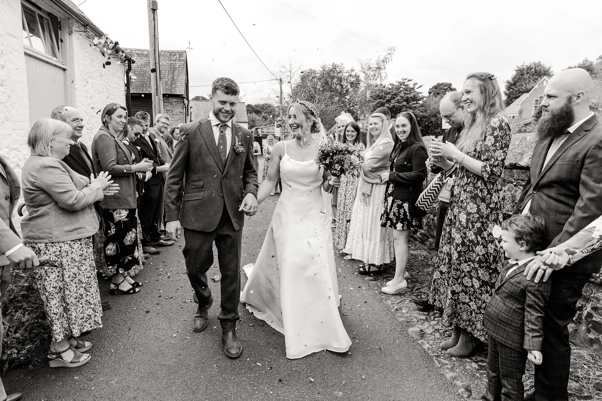 Newlyweds walk through guests, smiling. A glorious Farm Wedding in Aldbourne, Wiltshire.
