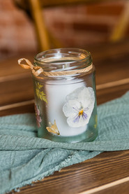 Glass jar candle decoration with white flower and floral prints on surface