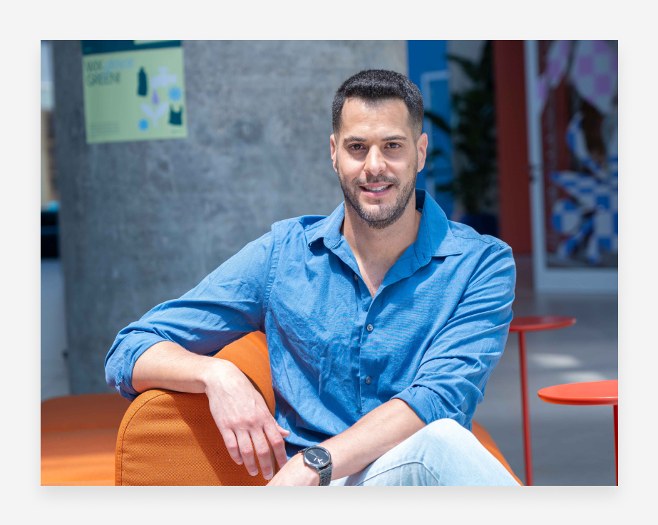 Ahi Ben-David wearing a blue shirt and posing on an orange couch.
