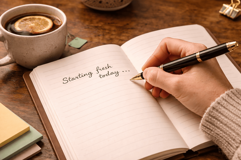 Close-up view of a hand writing in a journal with a cup of tea nearby