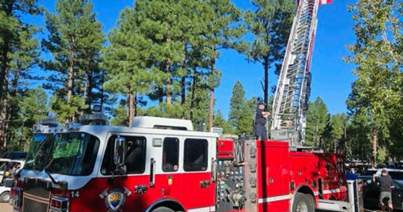 Fire truck raising the American Flag on fire ladder with pine trees in the background