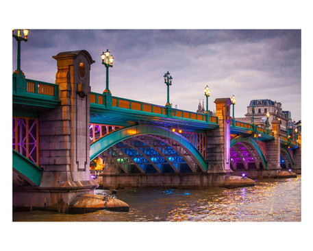 A vibrant evening photograph of Southwark Bridge in London by Janusz Miarka, illuminated with colorful blue, purple, and golden lights reflecting on the River Thames.