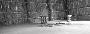 A traditional living space in a village in Sexaxa, Botswana, with woven reed walls, wooden stools, and firewood arranged on the ground. A minimalist setting that reflects cultural traditions. Captured by Janusz Miarka.