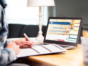 Person completing an online application while working at a desk beside a laptop displaying an application webpage.