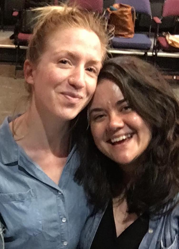 Two women smile at the camera - both wear denim shirts; the one on the left is taller and blond, the one on the right is shorter and has brown hair
