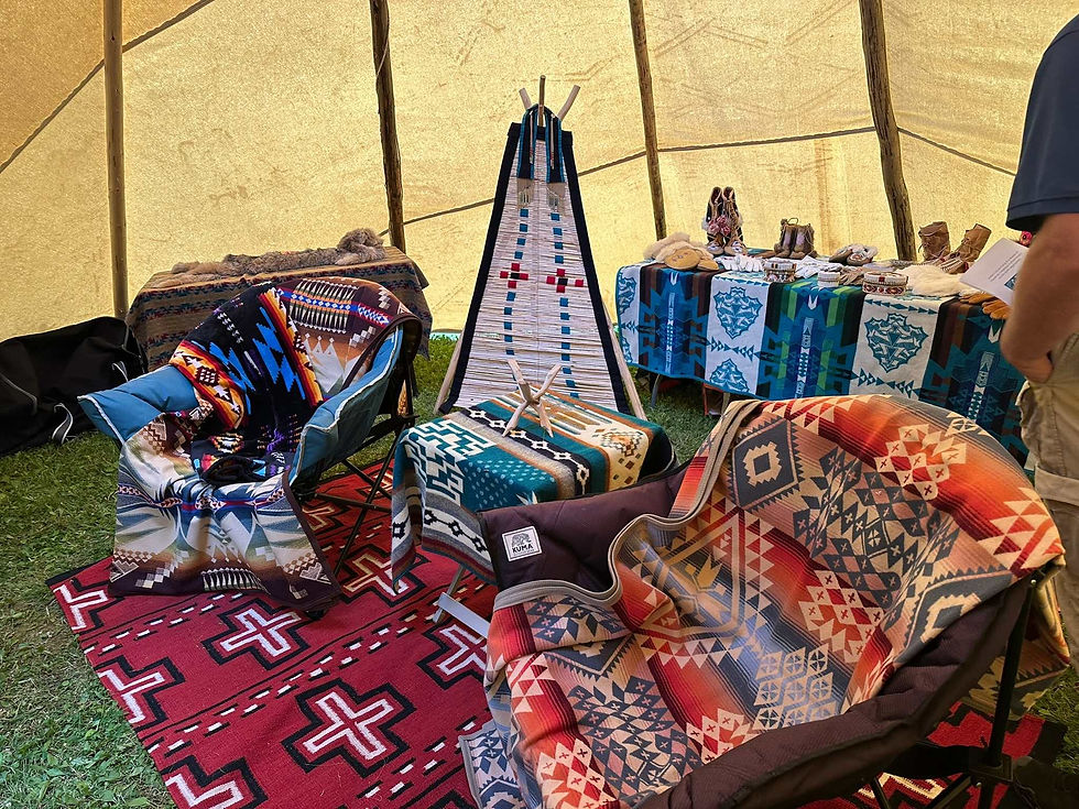 a number of colourful Indigenous artifacts sit inside a teepee. It includes many blankets and clothing.