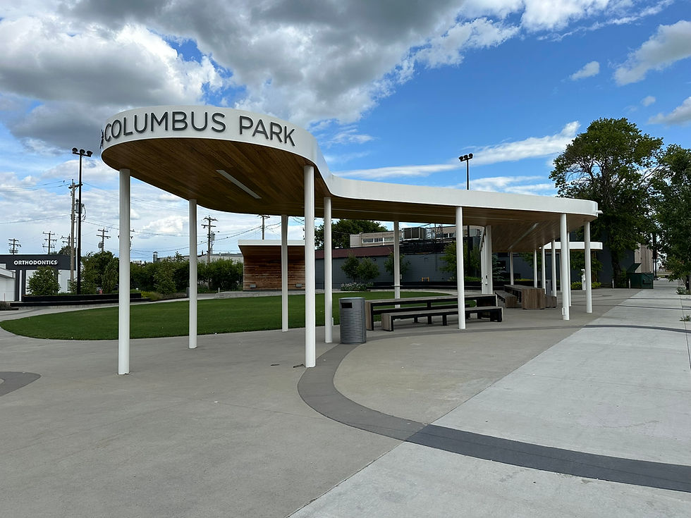 This is an image of Columbus Park. It shows the name of the Park. It is showing the covered shelter where people can sit under at tables and watch live performances. I the backgroundf is the new entertainment stage.