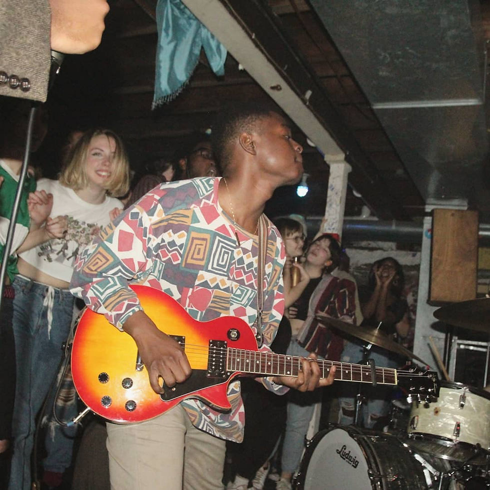 Miloe playing an electric guitar at a show, crowd members smiling behind him, drum kit behind him.