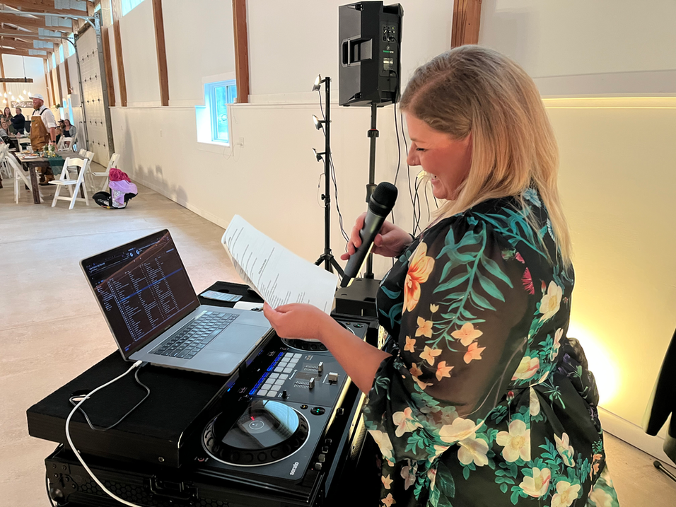 DJ Lindsay smiling, holding mic and paper at an event