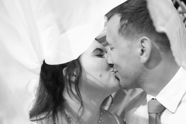 Bride and groom kissing under a white veil
