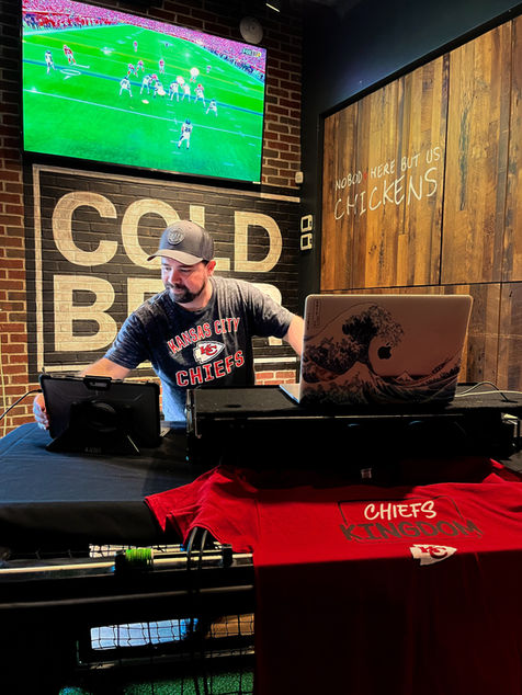 DJ Caleb in Chiefs shirt with equipment, football game playing.