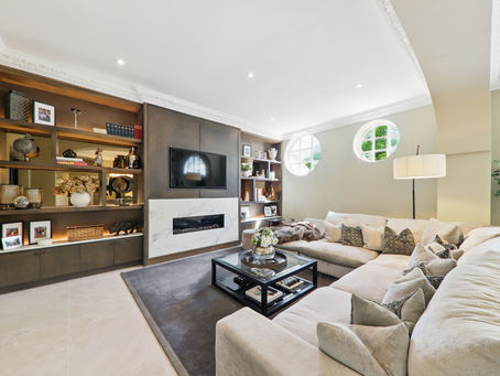Cozy living room with beige sectional, patterned pillows, a black coffee table, built-in shelves, and a wall-mounted TV. Circular windows give soft light.