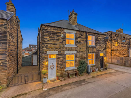 Stone row houses at dusk with warm lit windows, blue sky, front doors and potted plants along a quiet street.