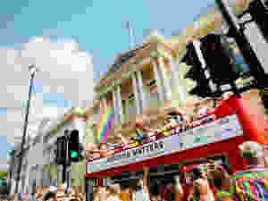 Red London bus with people holding rainbow flags.