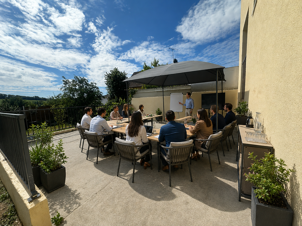 Réunion professionnelle en terrasse, grande table rectangulaire, plusieurs personnes assises, présentateur debout devant un tableau blanc, ciel bleu avec nuages, format paysage