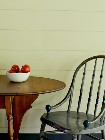 A windsor chair next to a drop leaf table with a bowl of fresh fruit