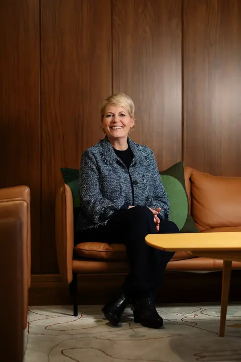Vibeke Fürst Haugen, head of Norwegian Broadcasting Corporation (NRK), sitting on a brown sofa in her office, with a brown wooden wall in the background.