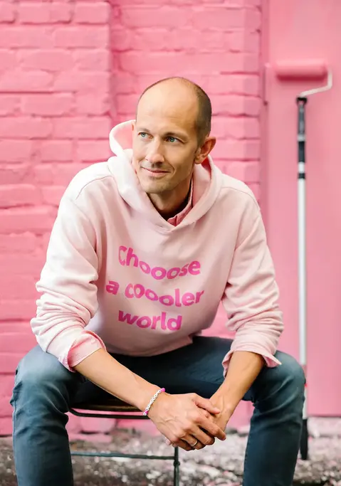 A portrait of Anders Slettvoll, founder of Chooose, sitting against a freshly painted pink wall with a paint roller behind him, wearing a pink jumper featuring the Chooose logo.