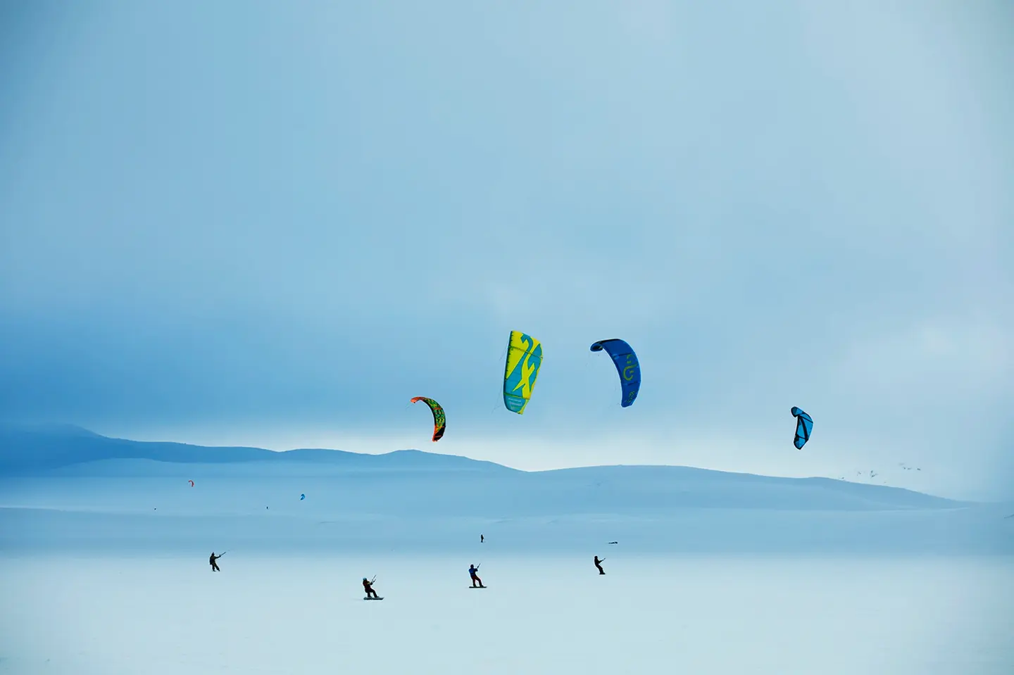 Four kiters against the snowy landscape of Hardangervidda, with the scenery almost appearing designed and surreal.