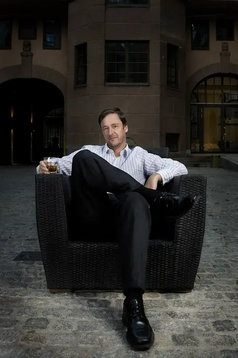 Portrait of Jon Christian Elden, famous Norwegian lawyer, sitting in a chair in the backyard of a building.