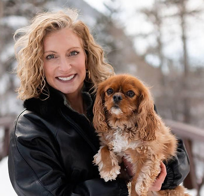 Lynn and her dog Rosie pose for a photo, framed by the stunning backdrop of the Colorado mountains dusted with snow.