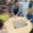 Teacher guides young children kneading dough on a round table.