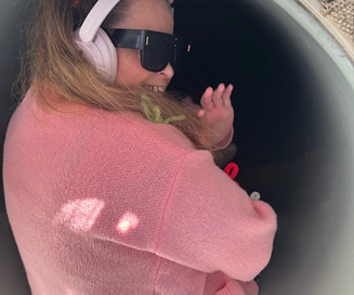Story of Courage: Just Wanting to Go on the Slide. Becky sitting at the top of the slide, turning back towards the camera smiling and waving, ready to go down the slide.