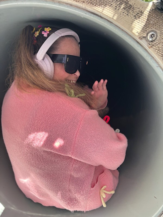 Becky's Blog 2 - Story of Courage: Just Wanting to Go on the Slide. Becky sitting at the top of the slide, looking back, smiling and waving, about to slide down.