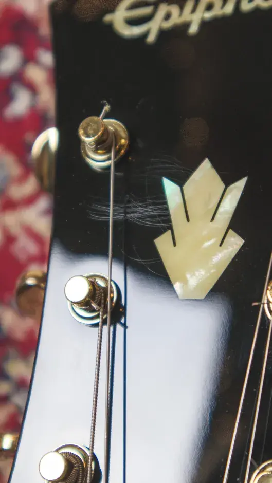 Thumbnail: Detailed view of light surface scratches on the headstock of the Epiphone Custom Riviera P93, with a carpet background for co