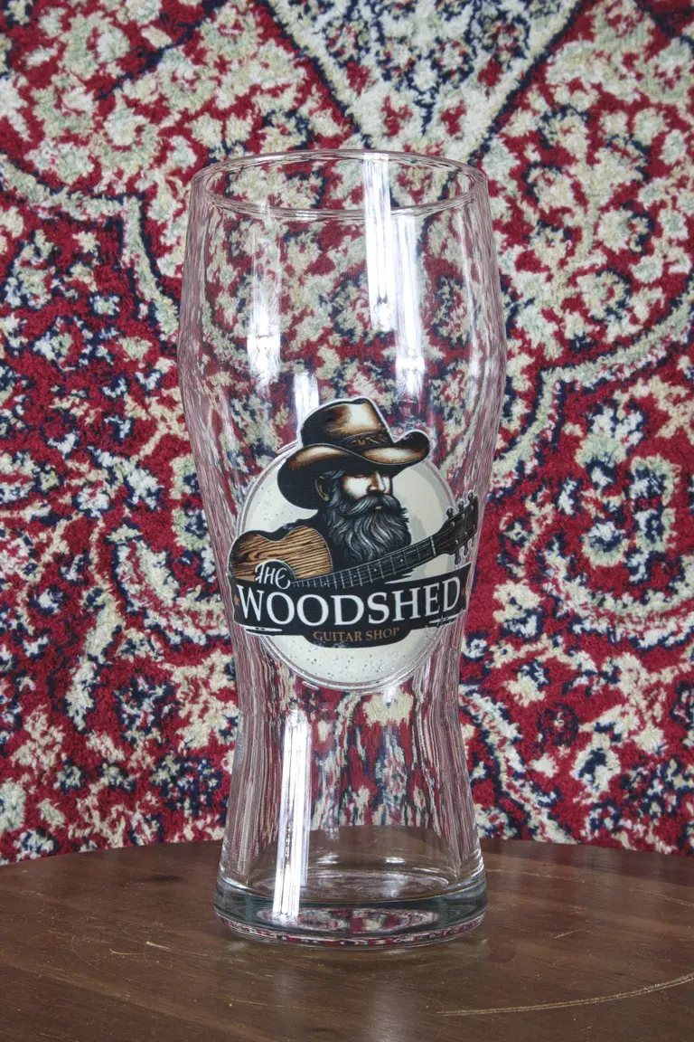 Woodshed pint glass with Reliced Americana logo on table.