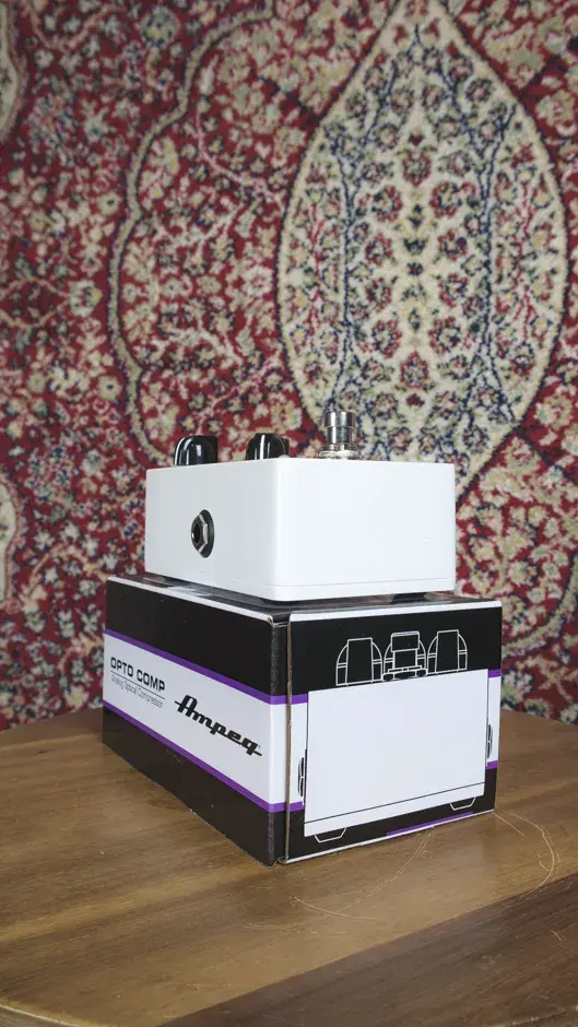 Ampeg Analog OPTO Comp pedal with its branded box displayed on The Woodshed's carpet backdrop