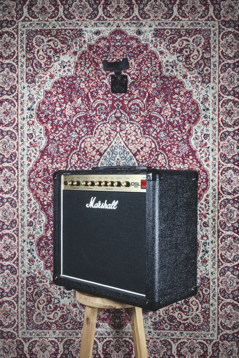 Angled front view of Marshall DSL15C amplifier on wooden stool with patterned rug background.