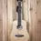 Thumbnail: Front view of a Tanglewood Travel Guitar TR2E on a timber wall hanger, showcasing its compact body and natural wood finish.